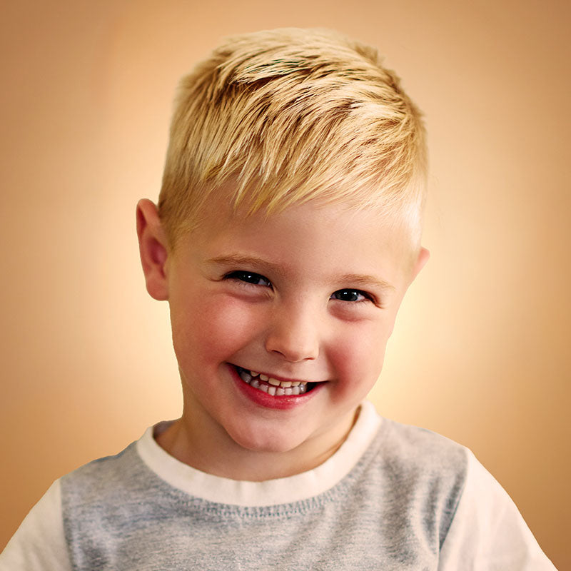 Young boy with blonde hair smiling against a beige background