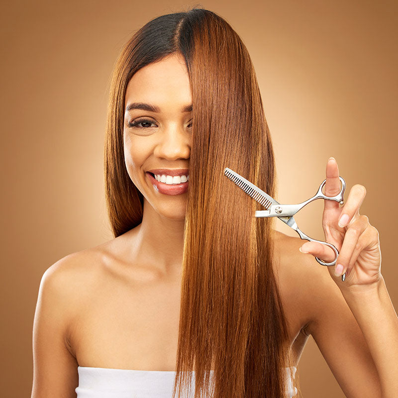 Woman with long, straight hair holding scissors against a brown background